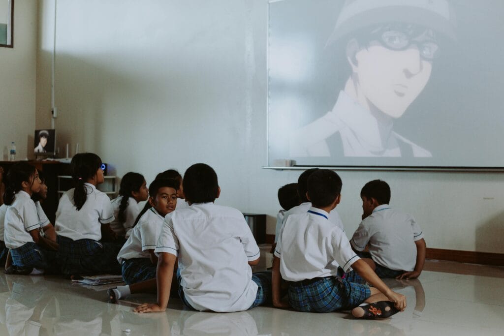 Young students in uniforms watch an educational video in a classroom setting.