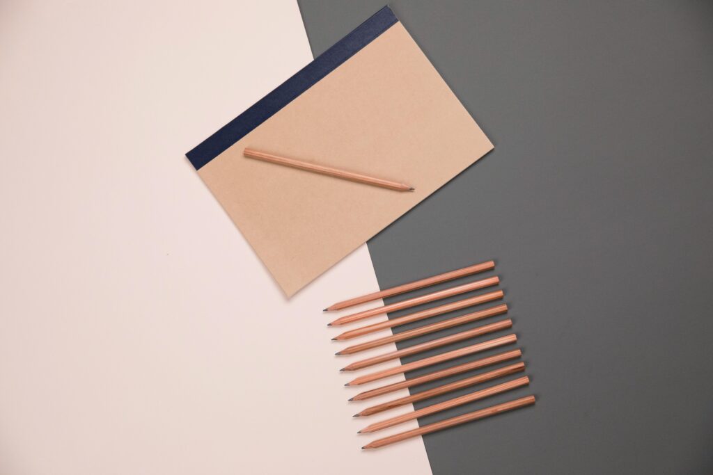 pexels photo 4417764 4417764 Top view set of various multicolored pencils placed on pink and gray table in row near sketchbook